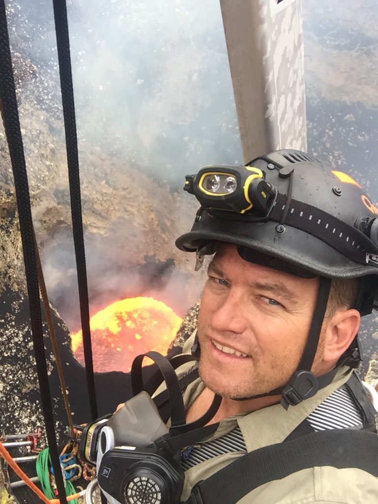 Mike Thompson in a climbing helmet and harness, above a volcano lava lake